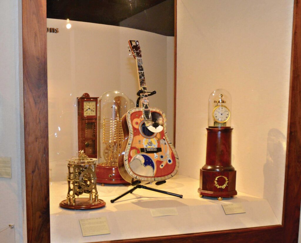 A clock-themed guitar inside a case with a orrery and lighthouse clock